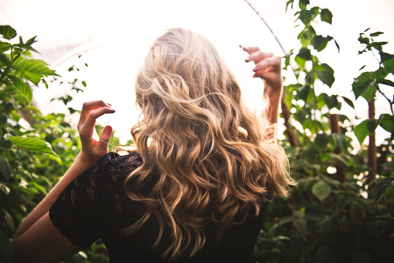 Home Blonde woman with curly hair surrounded by lush greenery, enjoying a sunny day.