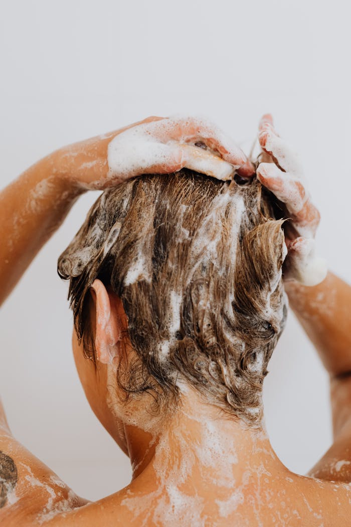 Close-up of a woman washing hair with foam shampoo, focused on hygiene and care.
